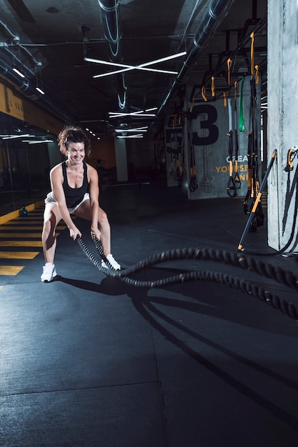 Mujer atlética feliz que ejercita con las cuerdas de la batalla en gimnasio