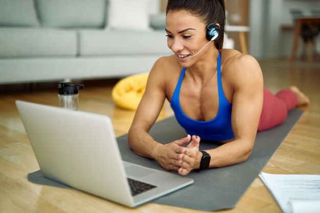 Mujer atlética feliz que usa una computadora portátil mientras tiene una clase de ejercicio en línea en casa