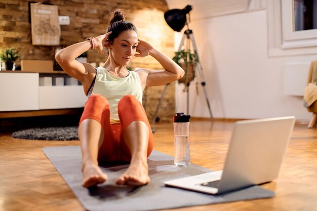 Mujer atlética haciendo sentadillas durante la clase de entrenamiento en línea en casa