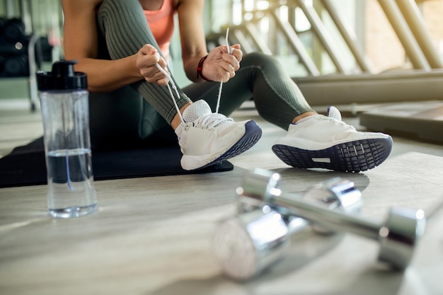 Mujer atlética irreconocible atando zapatos deportivos en el club de salud