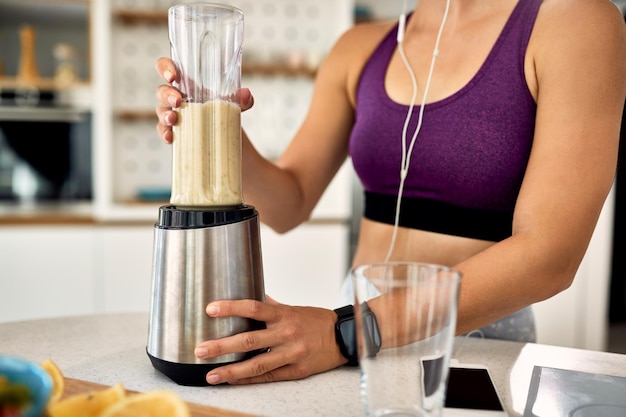 Mujer atlética irreconocible que usa licuadora mientras prepara un batido saludable en la cocina