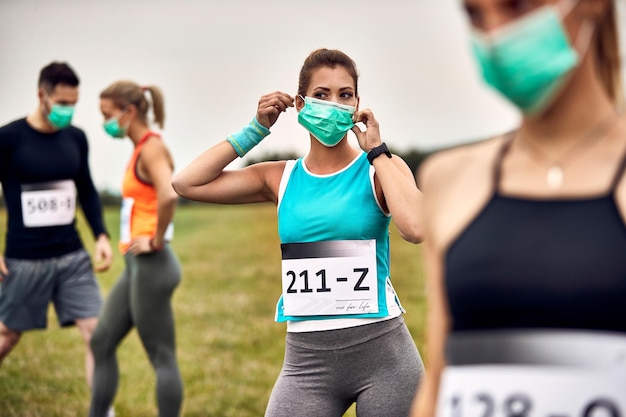 Mujer atlética preparándose para un maratón y poniéndose una máscara protectora en la naturaleza