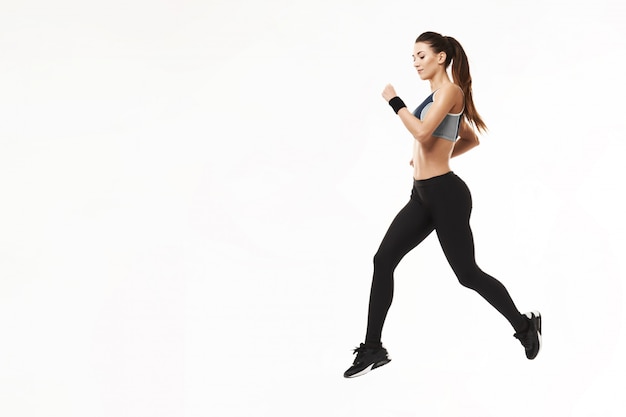 Mujer atlética en ropa deportiva entrenamiento corriendo en blanco.