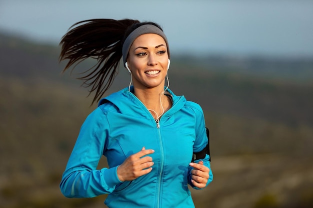 Mujer atlética sonriente trotando por la mañana y escuchando música con auriculares