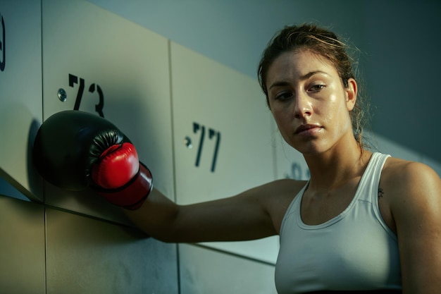 Mujer atlética sudorosa pensando en algo en el vestuario del gimnasio después del entrenamiento de boxeo