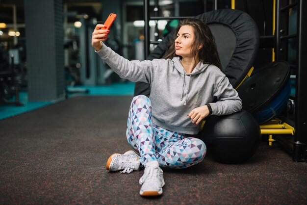 Mujer atlética tomando selfie en smartphone en gimnasio