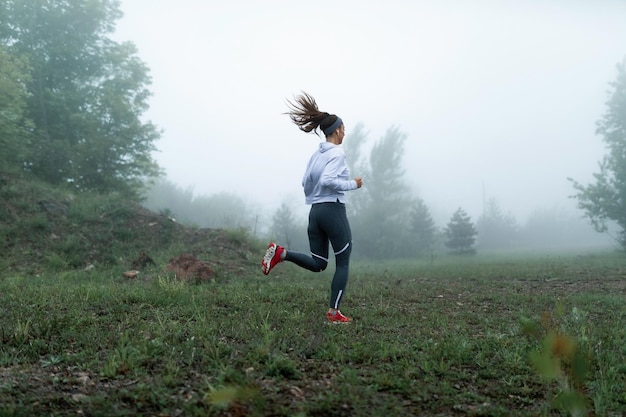 Mujer atlética trotando en la naturaleza en la mañana nublada y escuchando música con auriculares Copiar espacio