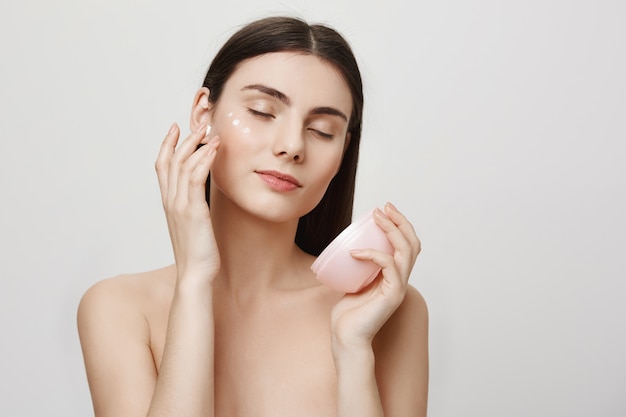 Mujer atractiva aplicar crema facial, producto anti-envejecimiento