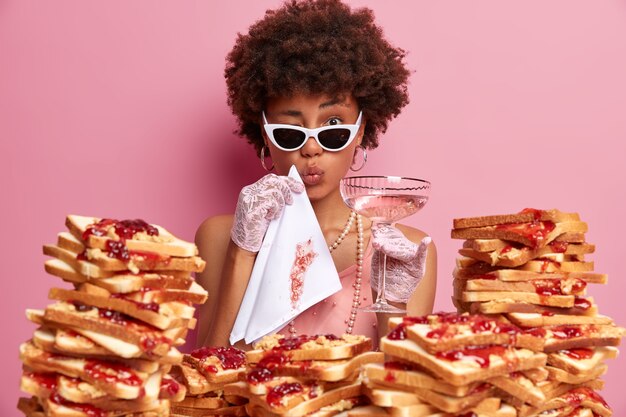 Mujer atractiva con cabello afro rodeado de sándwiches de gelatina de mantequilla de maní