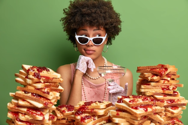 Mujer atractiva con cabello afro rodeado de sándwiches de gelatina de mantequilla de maní