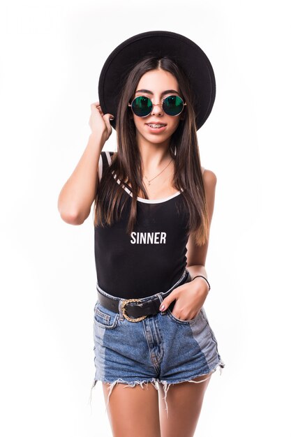 Mujer atractiva en camiseta negra jeans pantalones cortos sombrero y gafas de sol posando.