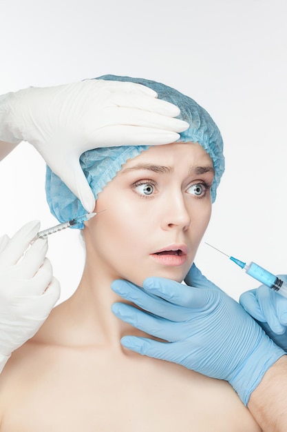 Mujer atractiva en cirugía plástica con jeringa en la cara sobre fondo blanco.