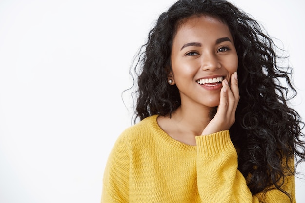 Mujer atractiva sin defectos, imperfecciones, tocando la piel pura y limpia y sonriendo con deleite, sintiendo felicidad, mirando la cámara con ternura