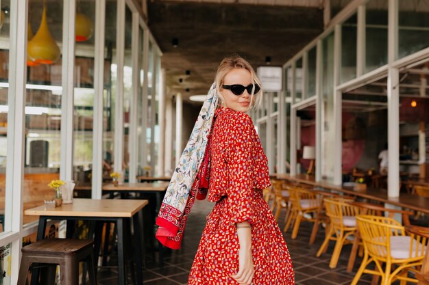 Mujer atractiva elegante caminando en vestido rojo de verano con accesorios en la cabeza en café de verano