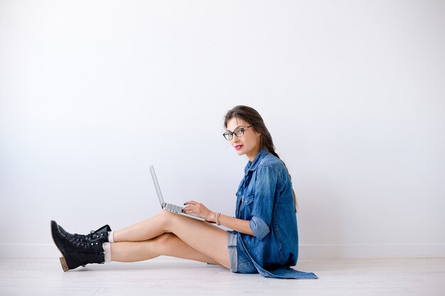 Mujer atractiva escribiendo en la computadora portátil mientras está sentado en el piso