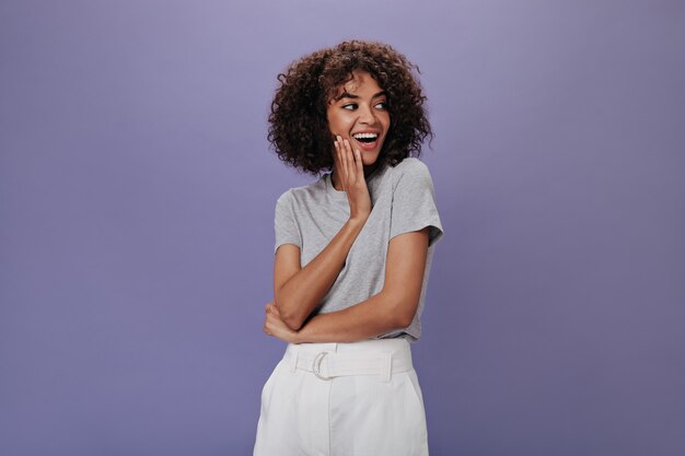 Mujer atractiva en falda blanca sonriendo y posando en la pared aislada