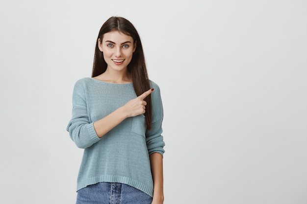 Mujer atractiva feliz que sonríe, señalando la esquina superior derecha en el anuncio