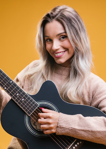 Mujer atractiva feliz que toca la guitarra contra fondo amarillo
