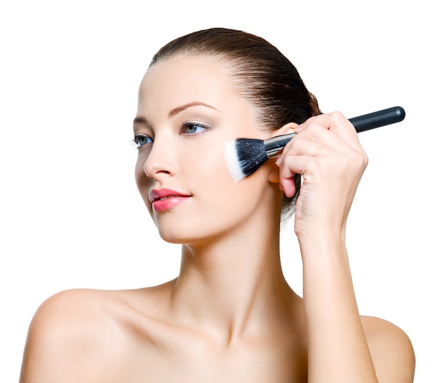 Mujer atractiva haciendo maquillaje en la cara. Modelo de moda posando sobre fondo blanco