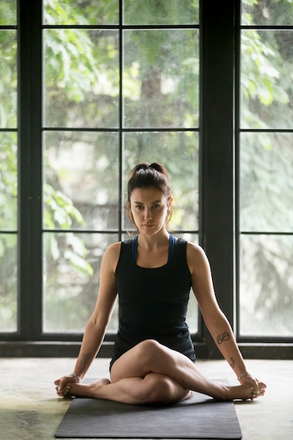 Mujer atractiva joven en la actitud de Gomukasana, fondo del estudio