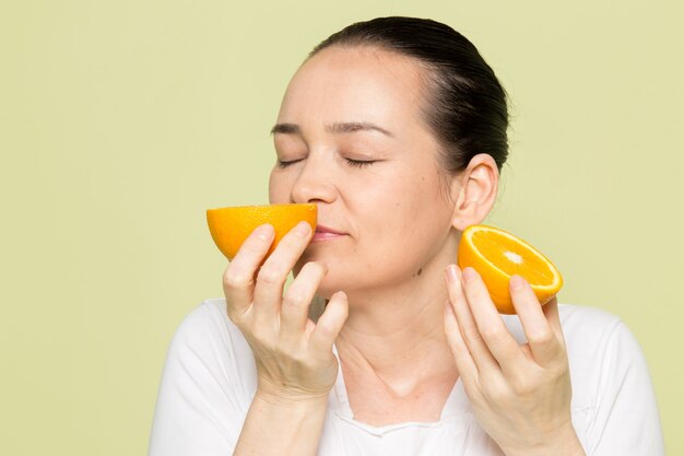 Mujer atractiva joven en camisa blanca que huele a naranjas plateadas