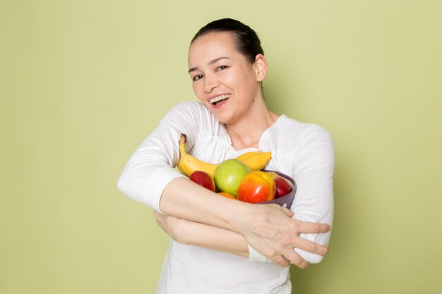Mujer atractiva joven en camisa blanca sonriendo y mostrando frutero