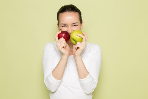 Mujer atractiva joven en camisa blanca sonriendo y sosteniendo manzanas verdes y rojas