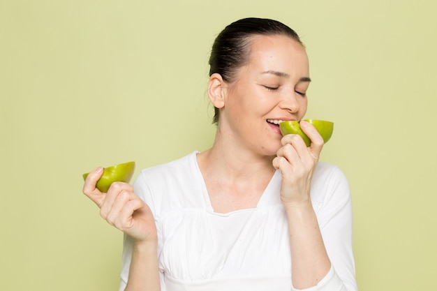 Mujer atractiva joven en camisa blanca sosteniendo y comiendo manzanas verdes en rodajas