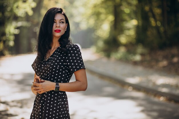 Mujer atractiva joven en elegante vestido de pie en el bosque