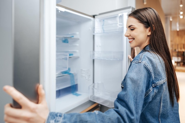 Mujer atractiva joven eligiendo frigorífico en hipermercado