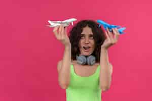 Foto gratuita una mujer atractiva joven feliz con el pelo corto en la parte superior verde de la cosecha en auriculares con aviones de juguete blancos y azules