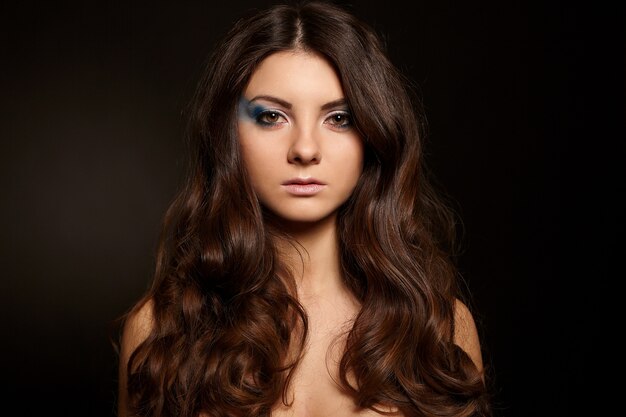 Mujer atractiva joven con maquillaje brillante largo cabello negro aislado sobre fondo negro