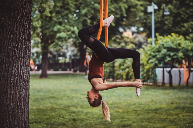 Mujer atractiva joven con el pelo largo está haciendo ejercicios en cabestrillo en el parque de verano.