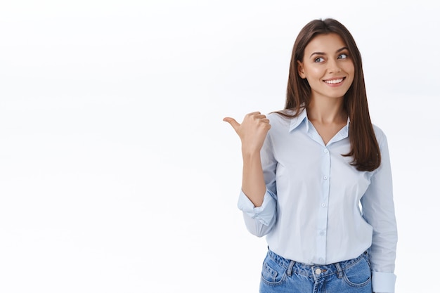 Mujer atractiva joven soñadora y complacida encontró exactamente lo que necesita, mirar y señalar a la izquierda satisfecho con una sonrisa feliz y encantada observar algo fresco, recomendar producto, pared blanca