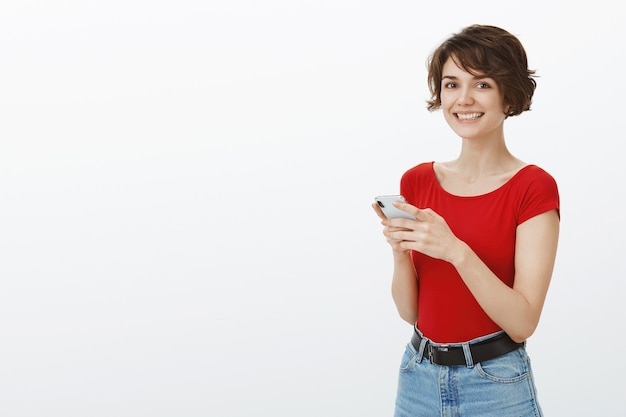 Mujer atractiva joven sonriente enviando mensajes de texto en el teléfono móvil, utilizando la aplicación de citas en el teléfono inteligente