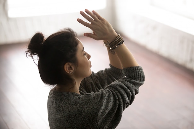 Mujer atractiva joven en suéter gris que hace namaste