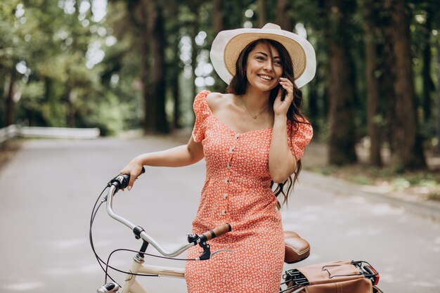 Mujer atractiva joven en vestido montando bicicleta y usando el teléfono