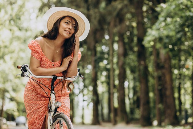 Mujer atractiva joven en vestido montando bicicleta y usando el teléfono
