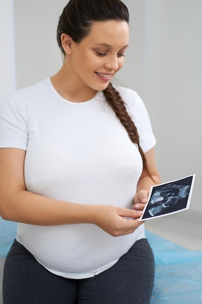 Mujer atractiva mirando fotos de ultrasonido en la clínica