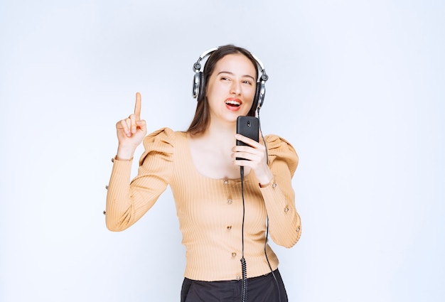 Una mujer atractiva modelo escuchando música en auriculares y apuntando hacia arriba.