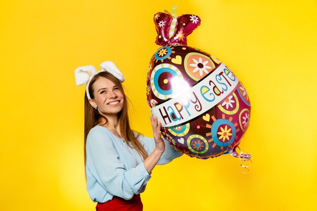 Mujer atractiva con orejas de conejo, jugando con globo de forma de huevo