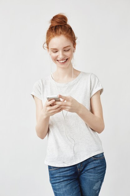 Mujer atractiva pelirroja con pecas sonriendo mirando el teléfono.