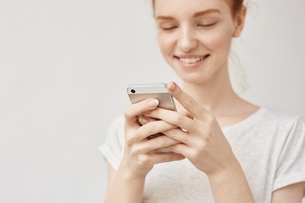 Mujer atractiva del pelirrojo que mira la sonrisa del teléfono de ar.