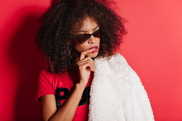 Mujer atractiva pensativa con piel oscura posando en gafas de sol