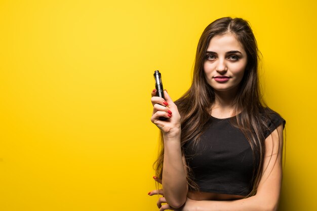 Mujer atractiva de pie y vaping en la pared amarilla.