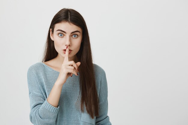 La mujer atractiva presiona el dedo a los labios pidiendo callar, callar