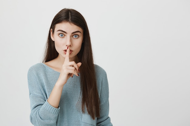 La mujer atractiva presiona el dedo a los labios pidiendo callar, callar