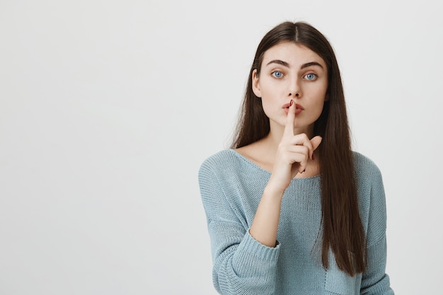 La mujer atractiva presiona el dedo a los labios pidiendo callar, callar