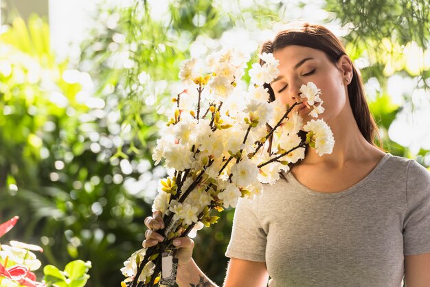 La mujer atractiva que sostiene el manojo de ramitas de la flor acerca a cara