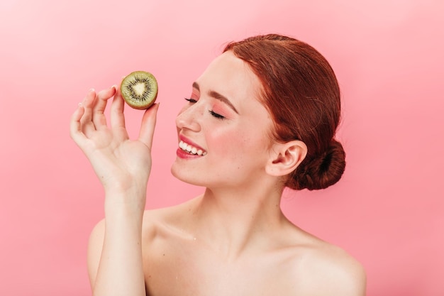 Mujer atractiva riendo sosteniendo kiwi Foto de estudio de una chica encantadora con frutas exóticas sobre fondo rosa